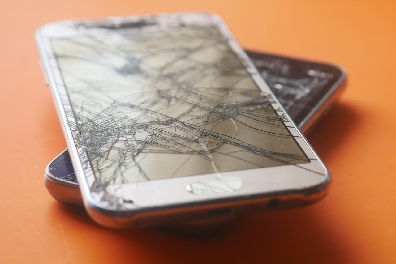 Two smartphones with cracked screens on an orange background