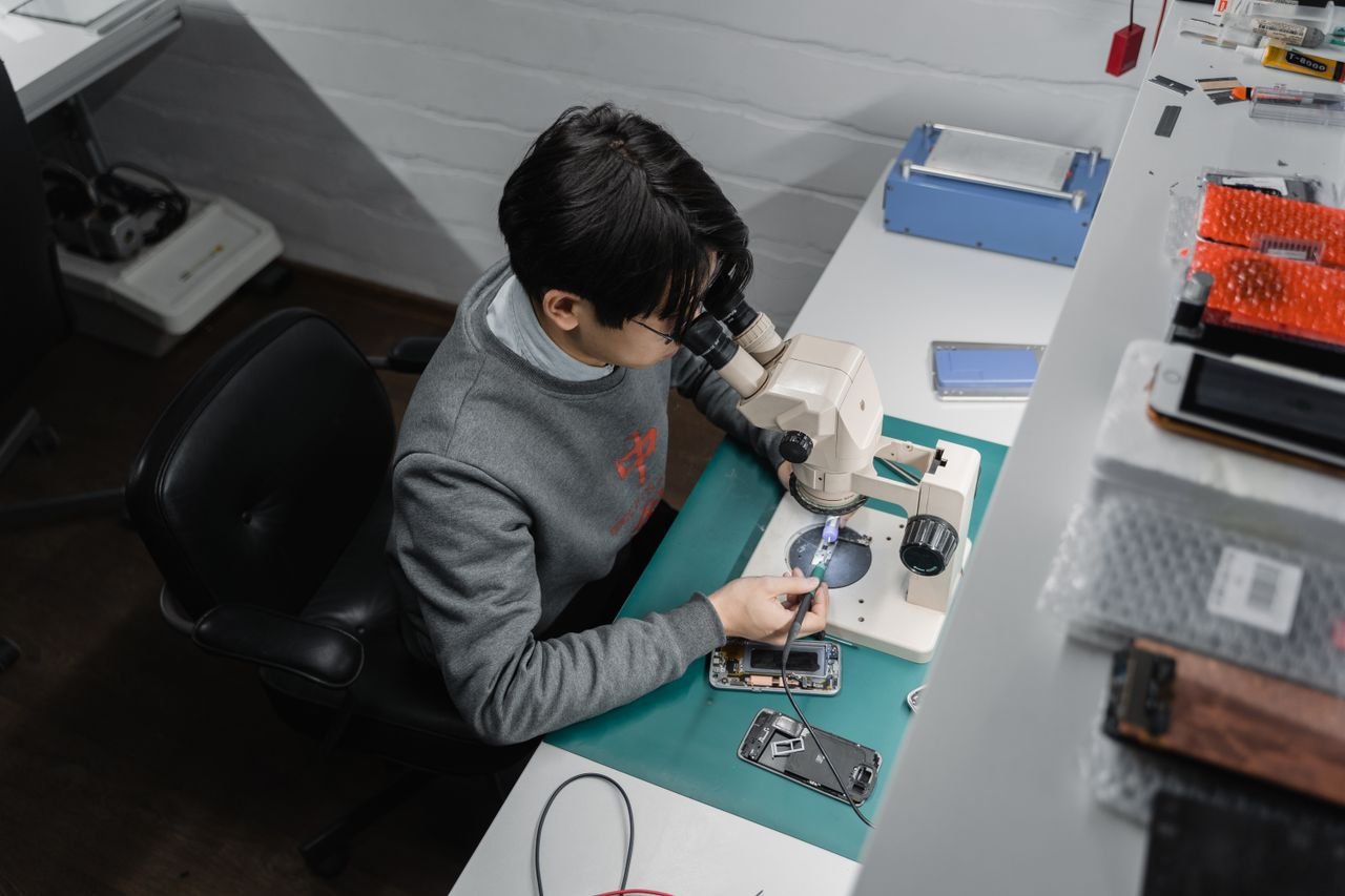 Certified technician repairing a phone under a microscope